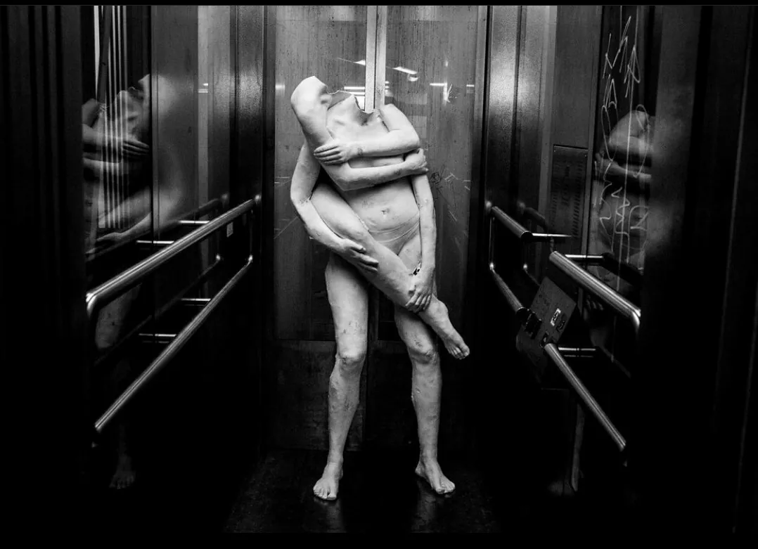 Two entwined full-body plaster figures in a lift